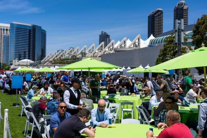 Tables and green umbrellas out on a lawn with convention center building in the nearby background